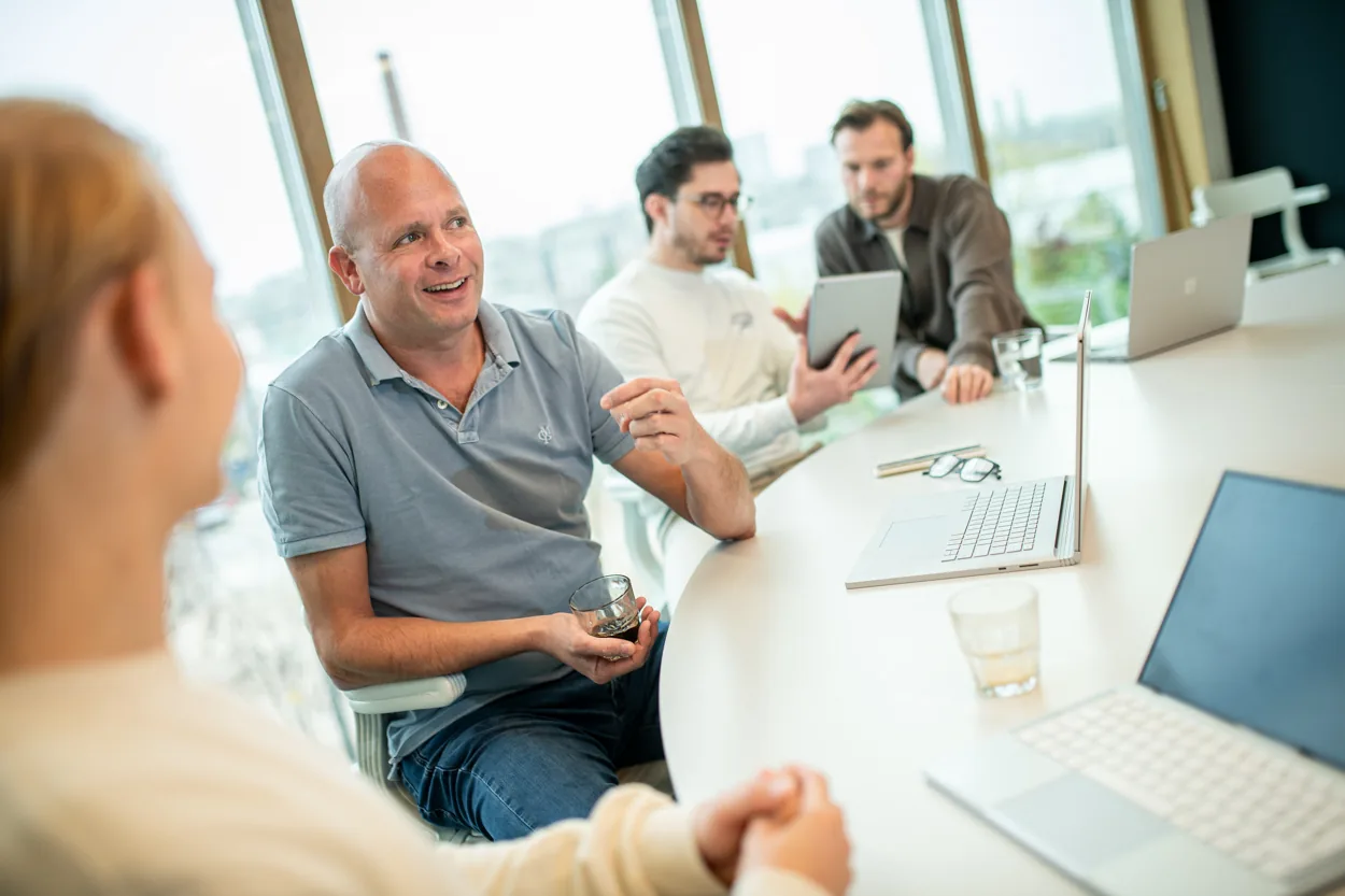Teamleden in gesprek aan een tafel met laptops en een tablet